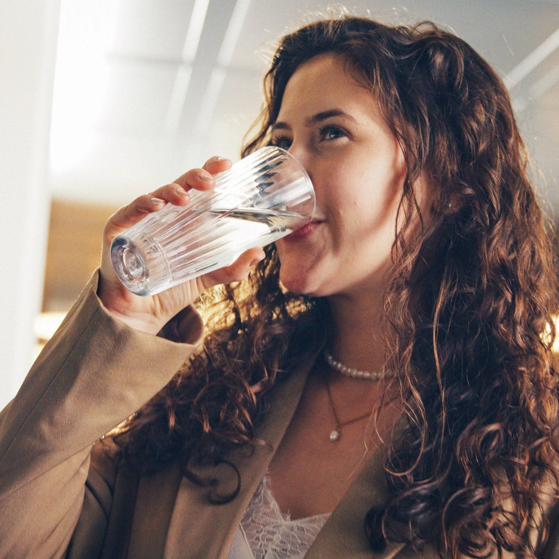 Una mujer bebiendo agua en el interior, con el fondo desenfocado