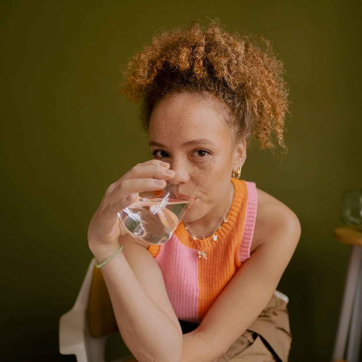 Una persona con un vaso de agua en la mano, con un fondo verde