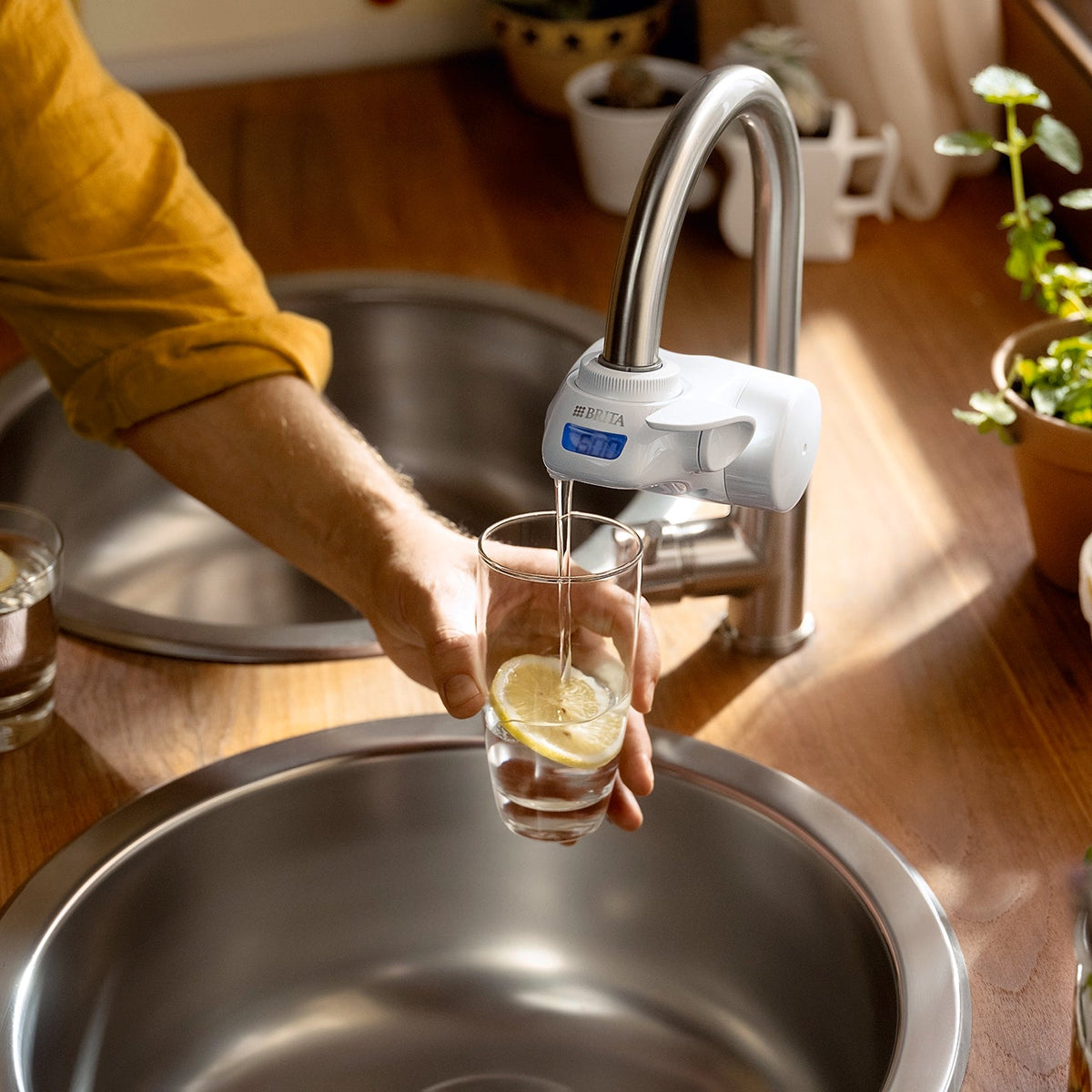 Glass with a lemon slice being filled with filtered water from a BRITA ON TAP Pro water filter system.